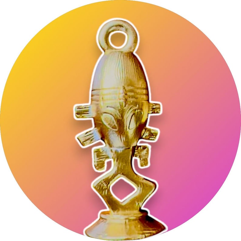 Puede incluir: Un colgante de metal dorado con un dise&ntilde;o de figura humana estilizada. La figura tiene una cabeza redonda con una cara y un cuerpo largo y delgado con brazos y piernas. El colgante tiene un bucle en la parte superior para colgar.