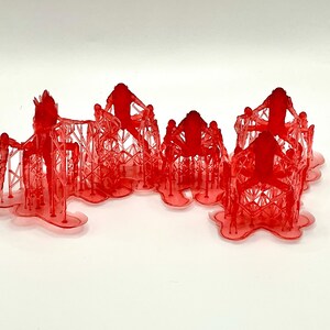 May include: A collection of six red, translucent miniature structures. Each structure has a figure on top of a geometric framework. The figures are posed with arms outstretched. The bases of the structures are joined.