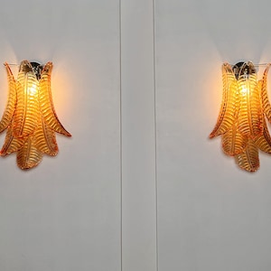 May include: Two amber glass wall sconces with a leaf design. The sconces are lit and casting a warm glow.