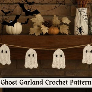 May include: A white crochet ghost garland with black eyes hangs in front of a fireplace mantel decorated for Halloween. The mantel features a white pumpkin, fall leaves, and a vase with a spider web design. The text "Ghost Garland Crochet Pattern" is at the bottom.
