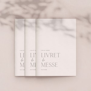 May include: Three off-white booklets with the text "LIVRET de MESSE" in a minimalist font. The names "LISA ET ADAM" and the date "18.07.2028" are also printed on the cover. The image has a soft, neutral color palette.