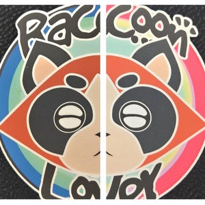 May include: A colorful sticker featuring a stylized raccoon face with the words "Raccoon Lover" in a playful font. The design includes a rainbow-colored background and a black outline.