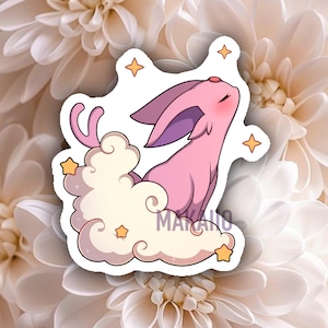 May include: A pink cartoon creature with large ears and a serene expression, resting on a cloud. The sticker features a light pink body, purple-lined ears, and is surrounded by yellow stars. The word "MAKANO" is visible on the sticker.