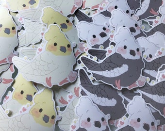 Puede incluir: Primer plano de una pila de pegatinas con cacatúas y palomas de dibujos animados. Las cacatúas son blancas con crestas amarillas y las palomas son grises con detalles blancos. Las pegatinas tienen corazones rosas y detalles de purpurina.