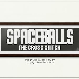 May include: A framed cross-stitch design with the words "SPACEBALLS" above "THE CROSS STITCH" in white block letters on a dark background. The frame is dark brown. Design size is 10.7 inches x 4 inches.