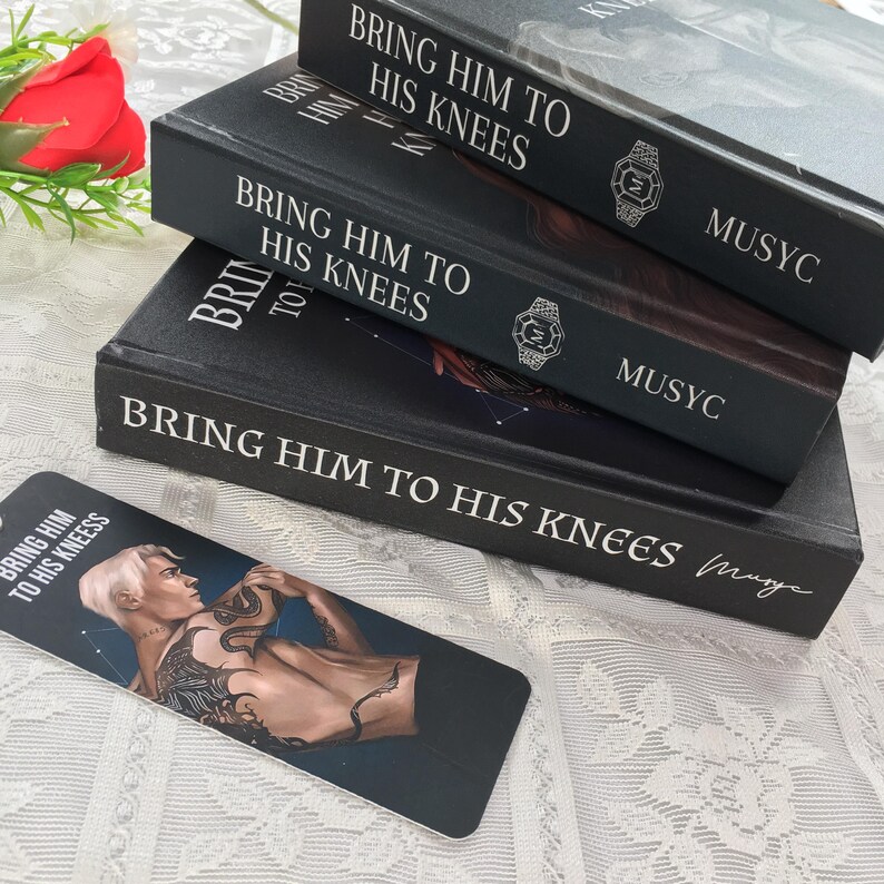 May include: Three black books stacked, titled "BRING HIM TO HIS KNEES" in white lettering. A bookmark with the same title and a male illustration is in front. The books have a watch design and the word "MUSYC".