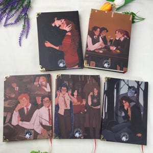 May include: A collection of five hardcover journals with illustrations of characters. The covers feature various scenes, including couples embracing and groups of people in a dining hall and library. Each journal has gold corner accents and a logo.