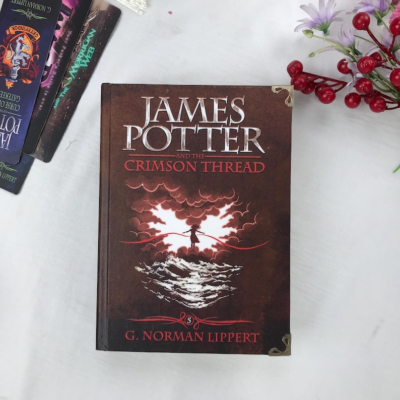 May include: A hardcover book titled "JAMES POTTER and the CRIMSON THREAD" with a brown cover. The cover features a silhouette of a person and red thread against a cloudy background. The book is part of a series by G. Norman Lippert.