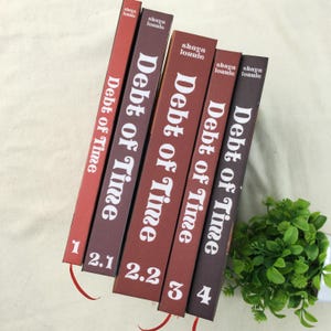 May include: A collection of five books with the title "Debt of Time" in white lettering. The book spines are various shades of red and brown. Numbers 1, 2.1, 2.2, 3, and 4 are visible on the spines. The author's name, "shaya lonule", is printed at the top.