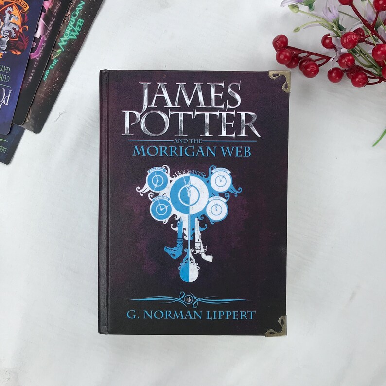 May include: A hardcover book titled "James Potter and the Morrigan Web" with a dark purple cover. The title is in silver lettering, and a blue and white clock-like design is featured. The author's name, G. Norman Lippert, is at the bottom.