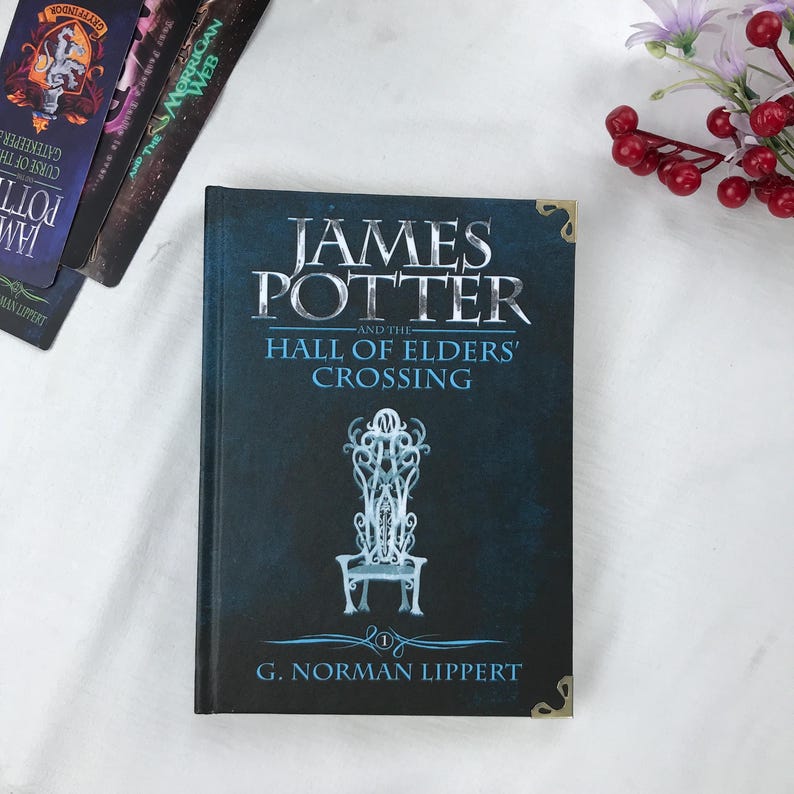 May include: A hardcover book titled "JAMES POTTER and the HALL OF ELDERS' CROSSING" by G. Norman Lippert. The cover is dark blue with silver lettering and a detailed illustration of a chair. Other books are visible in the background.
