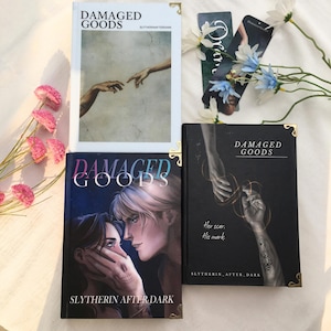May include: Four books with the title "DAMAGED GOODS" are displayed. Two books feature illustrations of hands, one with a Renaissance-style image. The other two books have illustrations of people. Bookmarks and flowers are also present.