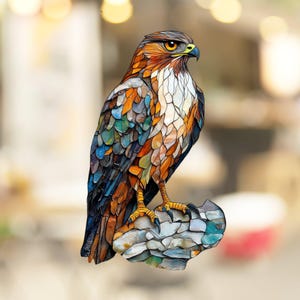 May include: A mosaic art piece of a hawk perched on a rock. The hawk is made of colorful glass tiles, with shades of blue, green, orange, and brown. The rock is also made of mosaic tiles, with shades of blue, green, and gray.