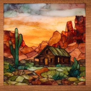May include: A colorful desert landscape painting featuring a wooden cabin with a green roof, a tall green cactus, and red rock formations under an orange and yellow sky. The artwork is framed in a wooden border.