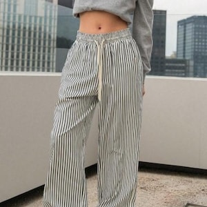 Puede incluir: Pantalón blanco con rayas verticales negras y cintura con cordón.