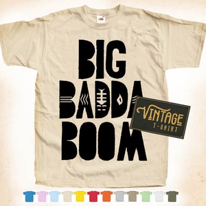 以下が含まれることがあります： ベージュのTシャツに、スタイリッシュなフォントで「BIG BADDA BOOM」と書かれた黒いグラフィックがプリントされています。Tシャツの右下にはヴィンテージラベルが付いています。