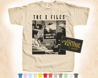 May include: A vintage beige t-shirt with a black and white image of the characters from the X-Files television show. The image includes the text "THE X FILES" and "I WANT TO BELIEVE". The t-shirt also has a black and white vintage label that says "VINTAGE T-SHIRT".
