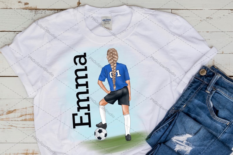 May include: White t-shirt with the name "Emma" printed in black on the left side. On the right side, a girl with blonde hair is wearing a blue soccer jersey with the number "01" on the back. She is holding a soccer ball and is standing on a green field.