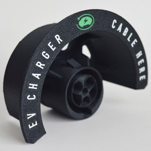 K&ouml;nnte beinhalten: Schwarzer EV-Ladeger&auml;t aus Kunststoff mit dem Text "EV CHARGER" und "CABLE HERE" in wei&szlig; gedruckt. Das Ladeger&auml;t hat ein gr&uuml;nes Logo mit einem Blitz darin.