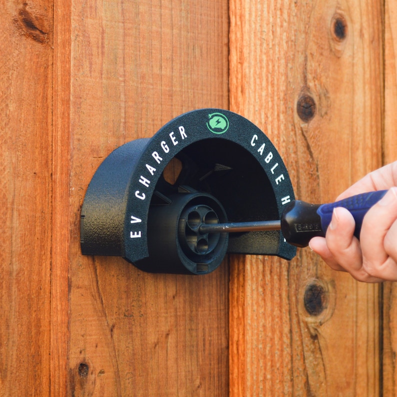 K&ouml;nnte beinhalten: Ein schwarzer Elektrofahrzeug-Ladeger&auml;t mit dem Text "EV CHARGER" und "CABLE H" darauf. Ein Schraubendreher wird verwendet, um eine Schraube am Ladeger&auml;t festzuziehen.