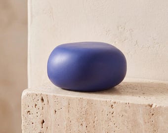 May include: A smooth, rounded, solid blue object with a matte finish. The item has a pebble-like shape with a uniform, deep blue color throughout its surface. It is a singular, compact piece with no visible markings, textures, or additional features.