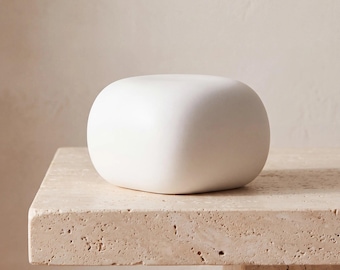 May include: A smooth, matte white object with a rounded, pebble-like shape. The item features a solid, opaque finish with soft, curved edges and a flattened top surface, presenting a clean and uniform appearance throughout its entire form.