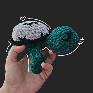 May include: A crocheted green and gray turtle toy. The turtle has a soft, fuzzy texture and is held in a person's hand.