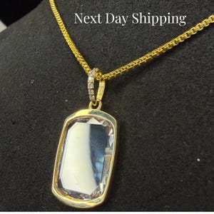 May include: A gold-toned necklace with a rectangular pendant. The pendant features a large, clear, rectangular stone set in a gold frame. The chain is also gold. The text "Next Day Shipping" is visible at the top.