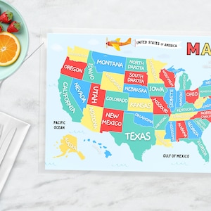 May include: A colorful map of the United States of America with each state labeled in a different color. The map is on a light blue background with a white border. The words "UNITED STATES OF AMERICA" and "MAP" are printed at the top of the map.