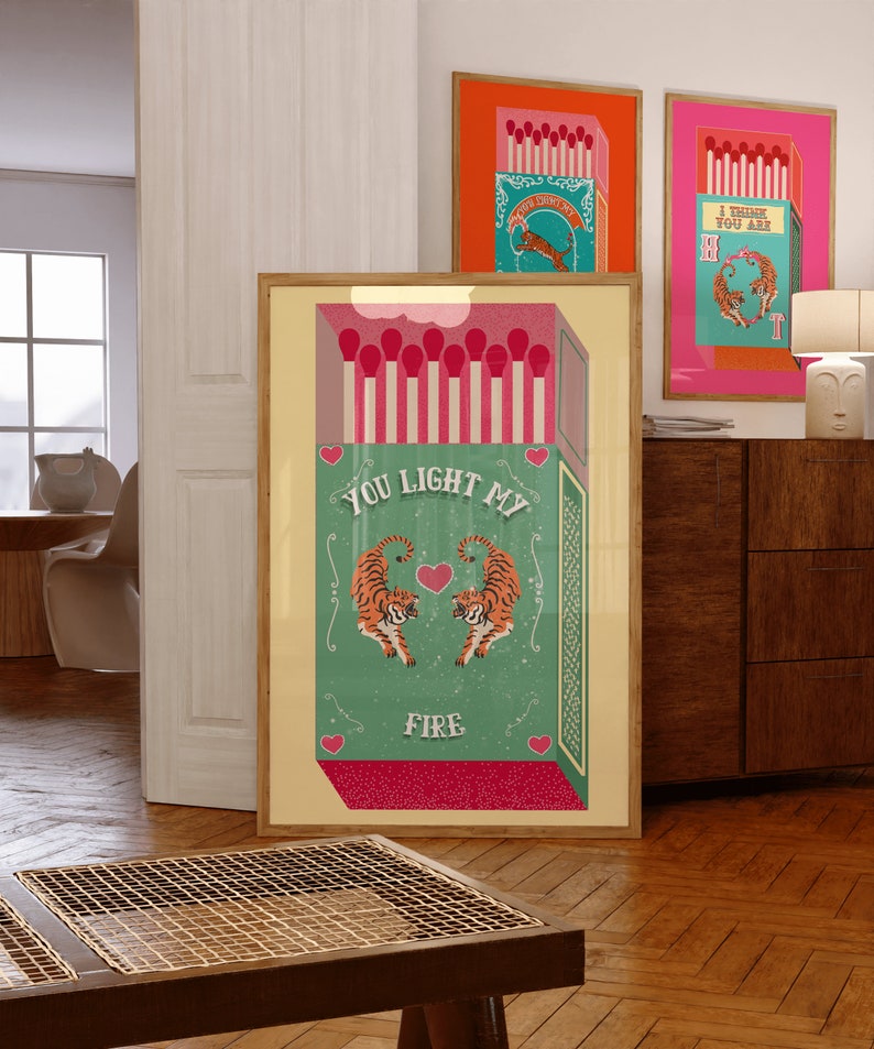 May include: A vintage-style illustration of a matchbox with two tigers facing each other. The matchbox is green with a red top and the text "You light my fire" is written in white. The tigers are orange and black with white stripes. The background is a light yellow.