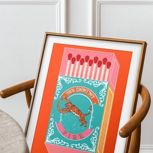 May include: A framed print with a red background featuring a matchbox with a tiger illustration and the text "You light my fire".