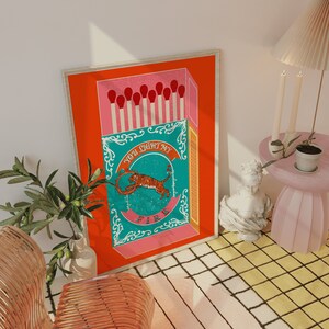 May include: A red and pink matchbox with a teal and white illustration of a tiger inside. The text on the matchbox reads "You light my fire".