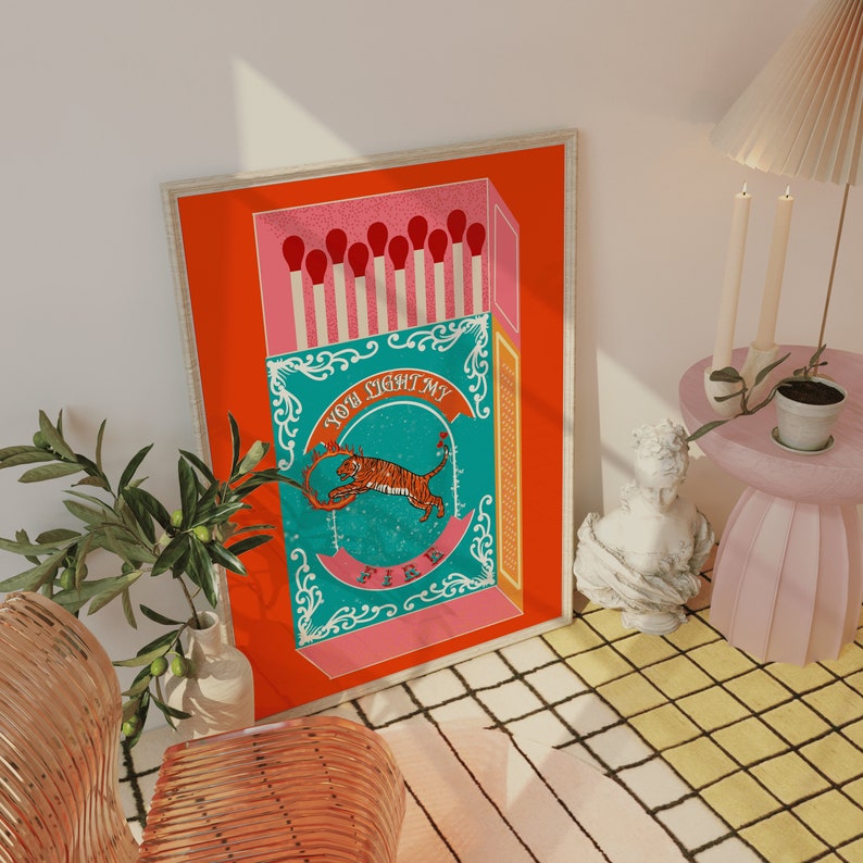 May include: A red and pink matchbox with a teal and white illustration of a tiger inside. The text on the matchbox reads "You light my fire".