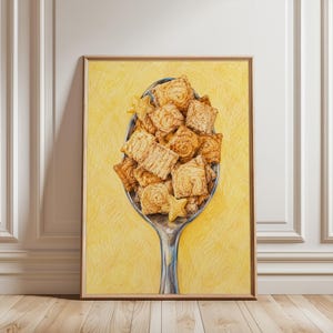 Pode incluir: Uma impressão de arte de parede vertical emoldurada apresentando uma colher de prata cheia de uma pilha de quadrados de cereais de canela dourados e duas pequenas peças em forma de estrela. O fundo é um amarelo vibrante e texturizado.