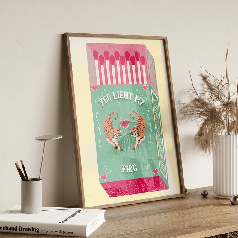 May include: A green and pink matchbox with two tigers facing each other. The text on the box reads "You light my fire".