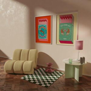May include: Two framed prints with a vintage aesthetic featuring illustrations of matchboxes with tigers and the text "You Light My Fire" and "You Light My Fire". The prints are hanging on a light pink wall above a light yellow couch and a green side table.