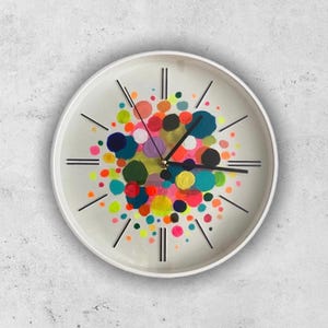 May include: A white round clock with black Roman numeral hour markers and black hands. The clock face is decorated with a colorful abstract design of various sized circles in shades of pink, yellow, green, blue, and red.