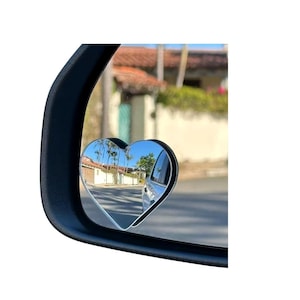 Op de afbeelding: Zwarte zijspiegel met een hartvormige dodehoekspiegel. De hartvormige spiegel reflecteert een straatbeeld met palmbomen en gebouwen onder een blauwe lucht. De hoofdspiegel is zwart.