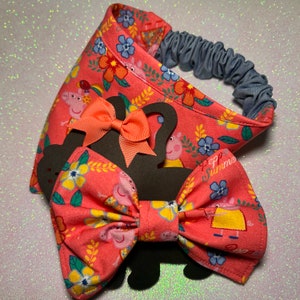 May include: A pink and green fabric bow tie and headband set featuring a cartoon pig character. The headband is made of denim and has an elastic band. The bow tie is tied with a large, bright orange bow.