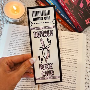 Może przedstawiać: Zakładka w kolorze r&oacute;żowym i czarnym z nożem i kapiącą krwią. Zakładka zawiera napis "Thriller Book Club" i "Crime Scene - Do Not Cross".