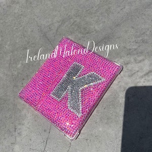 May include: A pink phone case with a clear back and a silver glitter letter K on the front. The case is covered in small pink glitter. The text "Ireland Malone Designs" is visible on the case.
