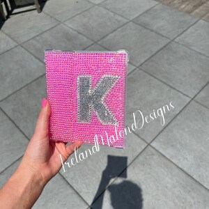 May include: A pink phone case with a silver letter K covered in rhinestones. The case is held in a hand. The text "Ireland Malone Designs" is visible in the bottom left corner of the image.