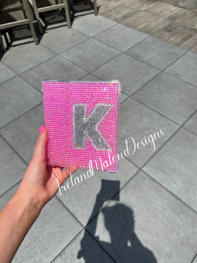 May include: A pink phone case with a silver letter K covered in rhinestones. The case is held in a hand. The text "Ireland Malone Designs" is visible in the bottom left corner of the image.