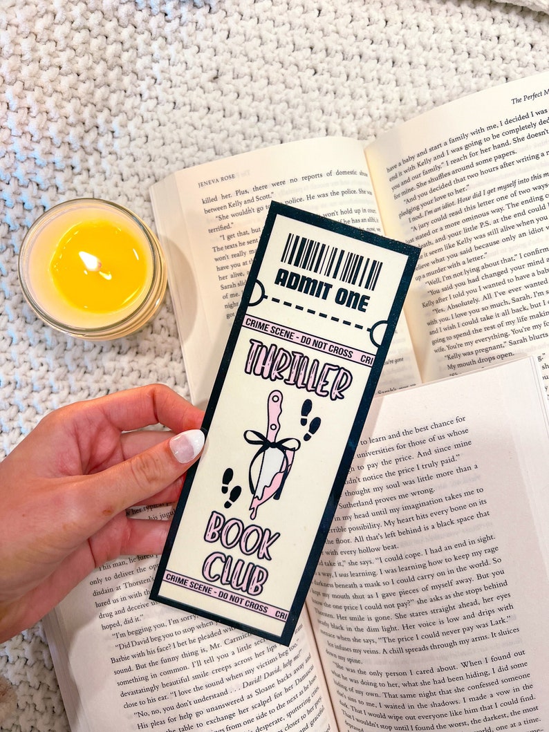 Może przedstawiać: Zakładka w kolorze r&oacute;żowym i czarnym z nożem i krwią kapiającą z ostrza. Zakładka zawiera napis "Thriller Book Club" i "Crime Scene - Do Not Cross".