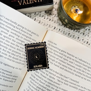 Puede incluir: Primer plano de un libro titulado "Awakening" de Susanne Valenti. El libro est&aacute; abierto en una p&aacute;gina con texto sobre una academia m&aacute;gica. Una pegatina con las palabras "Zodiac Academy" y "Solaris" est&aacute; en la p&aacute;gina. La pegatina es negra con una luna creciente y estrellas.