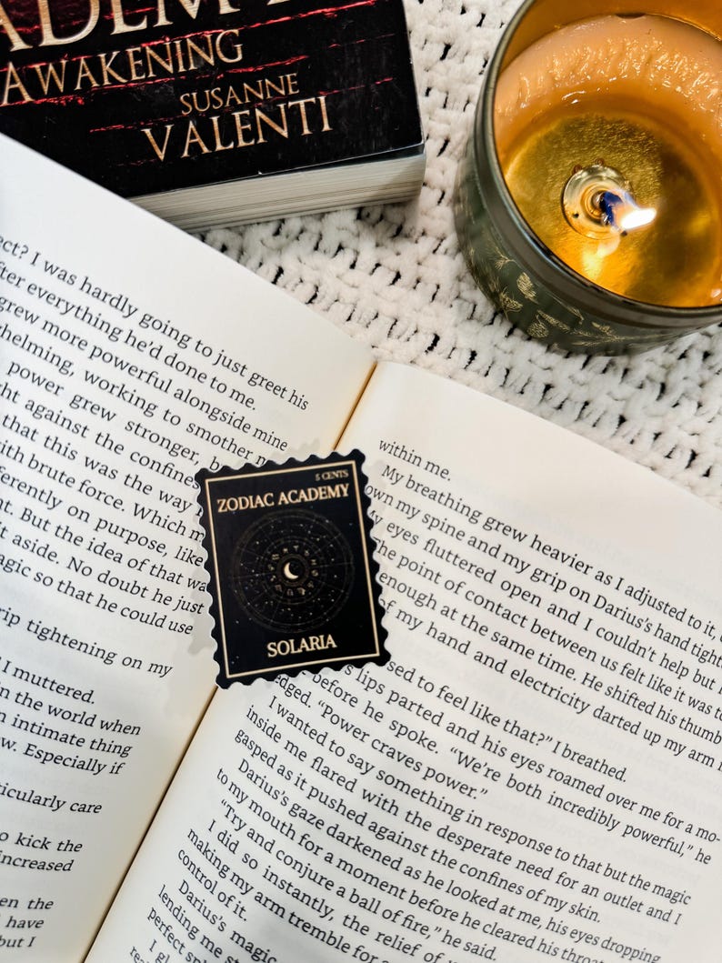 Puede incluir: Primer plano de un libro titulado "Awakening" de Susanne Valenti. El libro est&aacute; abierto en una p&aacute;gina con texto sobre una academia m&aacute;gica. Una pegatina con las palabras "Zodiac Academy" y "Solaris" est&aacute; en la p&aacute;gina. La pegatina es negra con una luna creciente y estrellas.