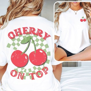 May include: White t-shirt with a red and green cherry graphic and the text "CHERRY ON TOP" printed on the back.