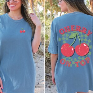 May include: A blue t-shirt with a cherry graphic on the front and the text "CHERRY ON TOP" on the back.