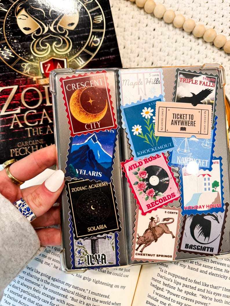 Puede incluir: Primer plano de una funda de tel&eacute;fono decorada con pegatinas coloridas. Las pegatinas presentan varios dise&ntilde;os, incluyendo una luna creciente, un horizonte urbano, un tocadiscos, una rosa salvaje y un billete que dice "Ticket to Anywhere".