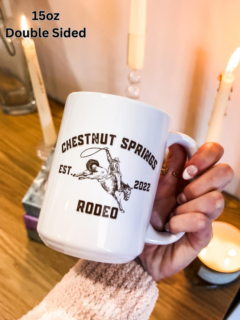 May include: White ceramic mug with a brown graphic of a cowboy riding a horse. The graphic includes the text "Chestnut Springs Est. 2022 Rodeo". The mug is 15 oz and double-sided.